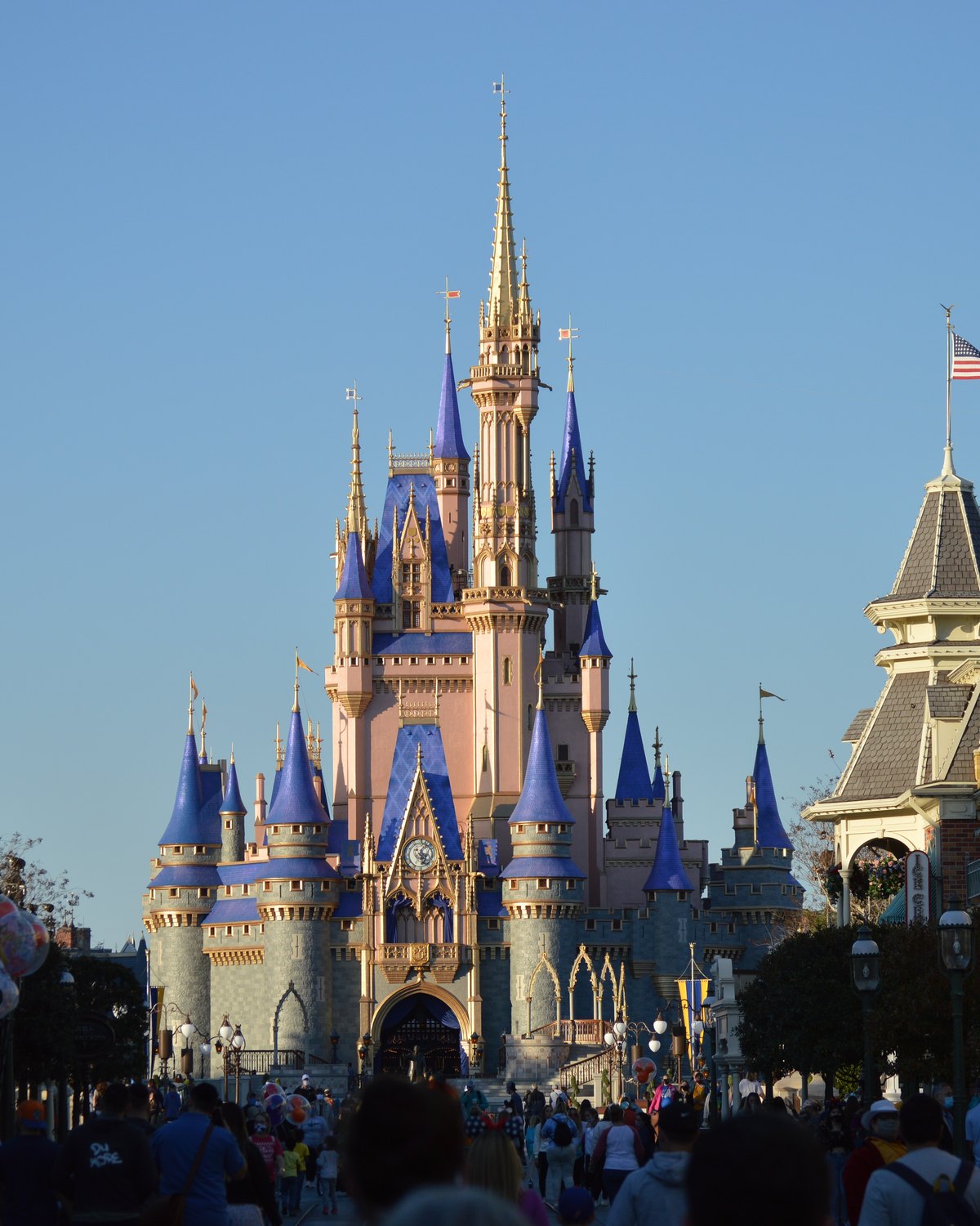 Castelo da Cinderela ao fim da Main Street do Magic Kingdom, em Orlando, sob céu azul e luz de dia, com visitantes caminhando em direção ao castelo