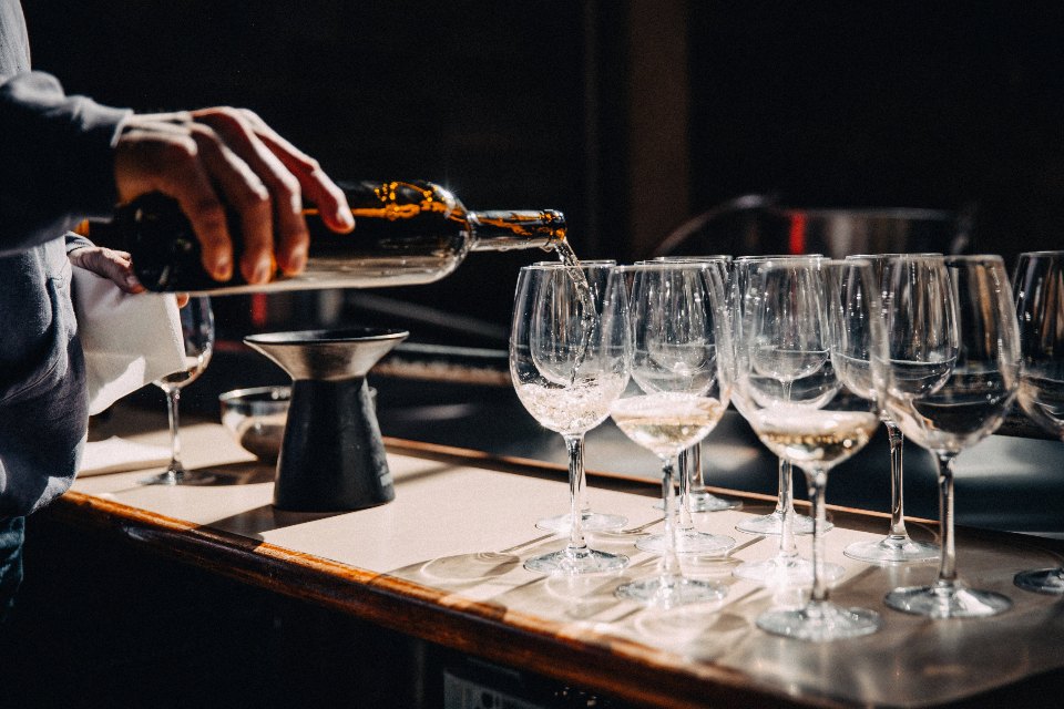 Sommelier servindo vinho em uma fileira de taças de cristal sobre a mesa